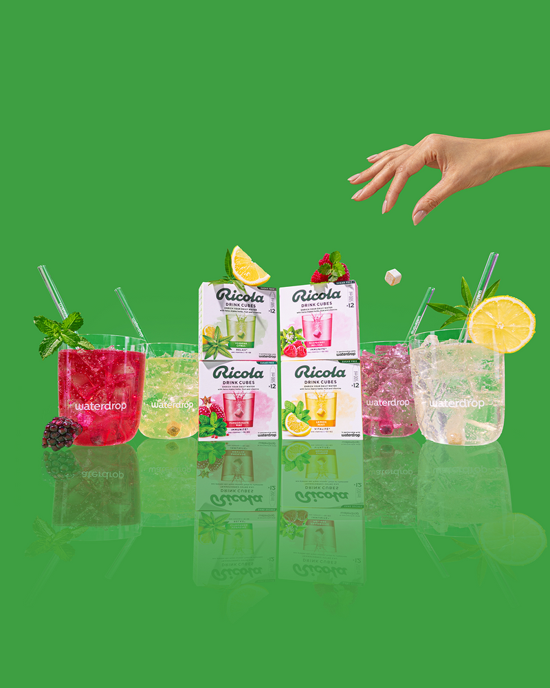 Smaki Ricola w szklankach. Ręka w prawym górnym rogu wrzuca kostkę napoju do szklanki.
