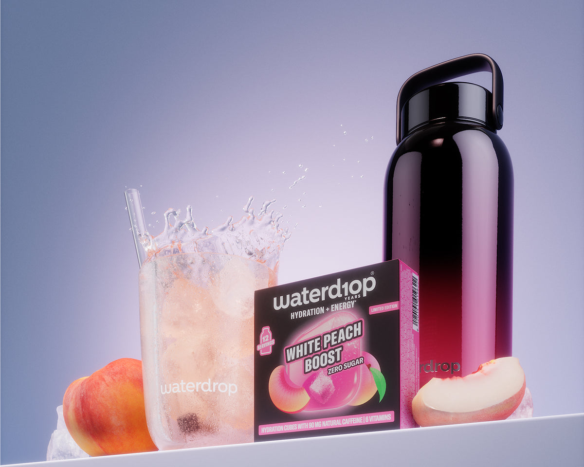 Pudełko produktu White Peach Boost obok szklanki z lodem i czarnej wielokrotnego użytku butelki na białej półce.