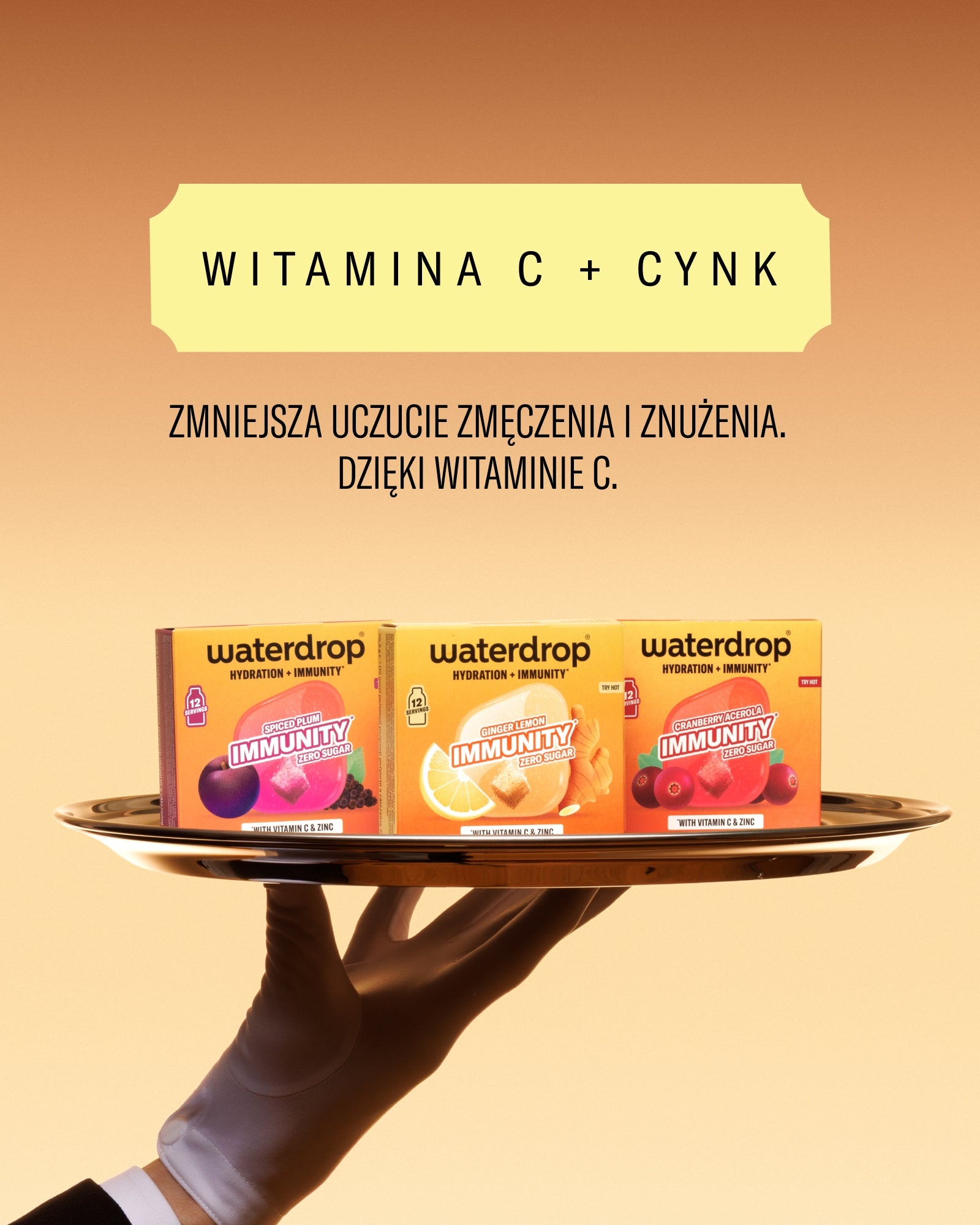 Dłoń trzyma złoty talerzyk z trzema pudełkami Waterdrop witamina C + cynk na pomarańczowym tle.